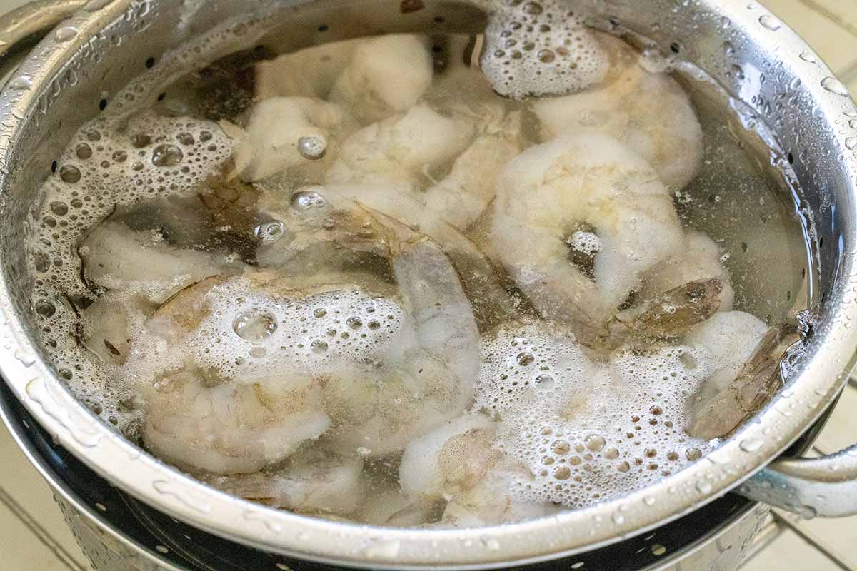 Pieces of frozen shrimp defrosting a bowl of water.