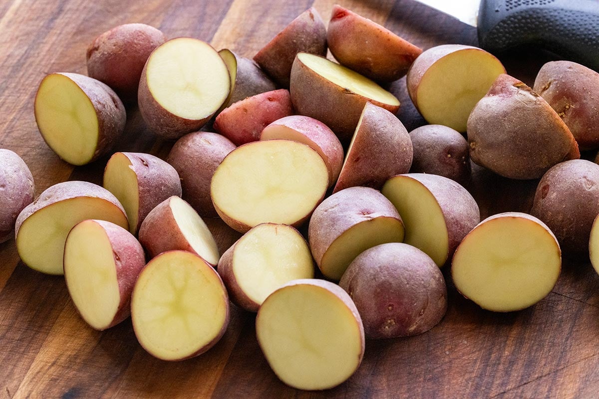 Red potatoes sliced in half on a wooden cutting board.