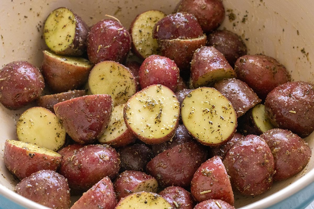Bowl of oil, seasoning, and sliced red potatoes.