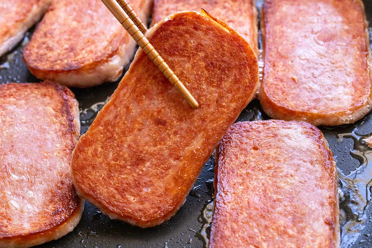 Slices of spam searing in a hot pan.