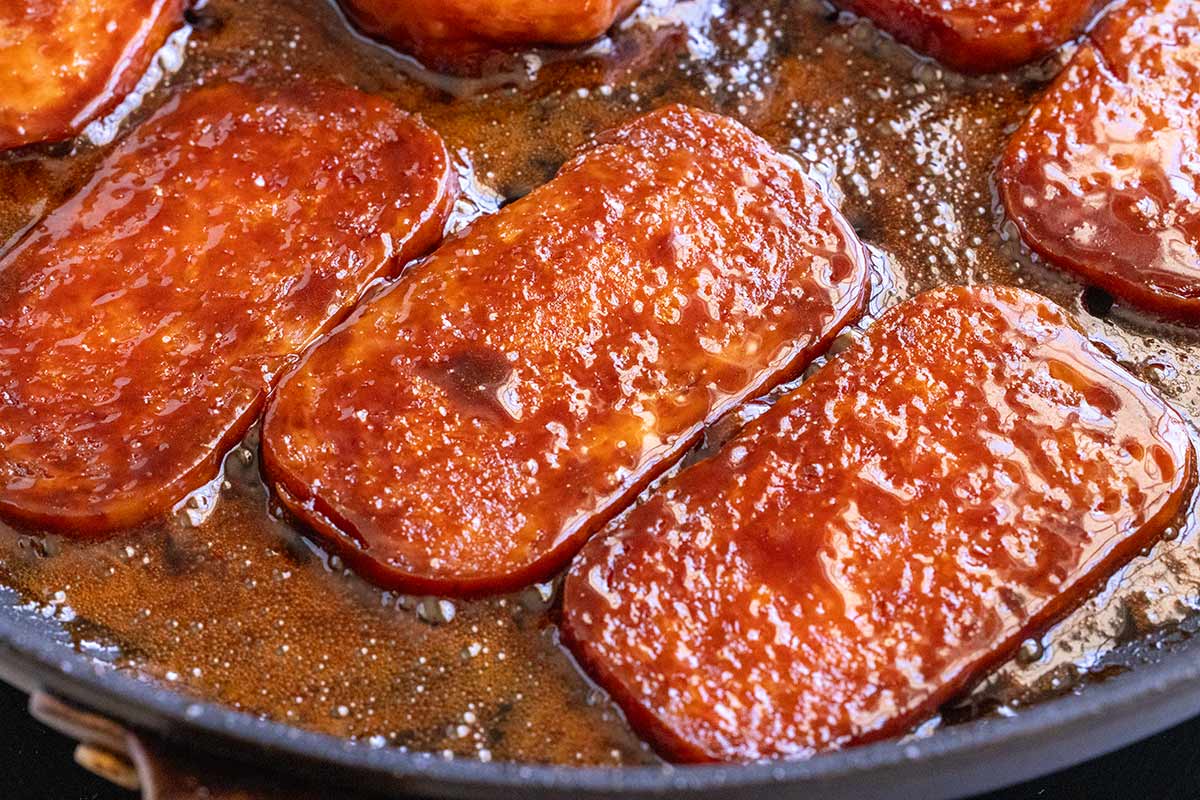 Spam cooking in a pan with glaze brushed on top.
