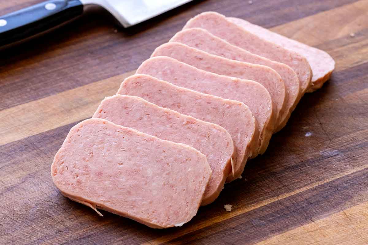 Slices of spam on a wooden cutting board.