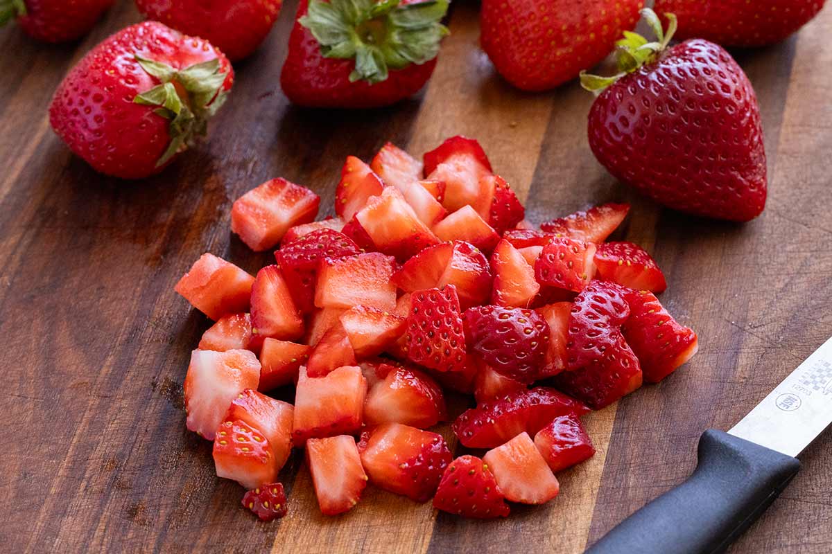 Fresh strawberries cut into pieces on a cutting board.