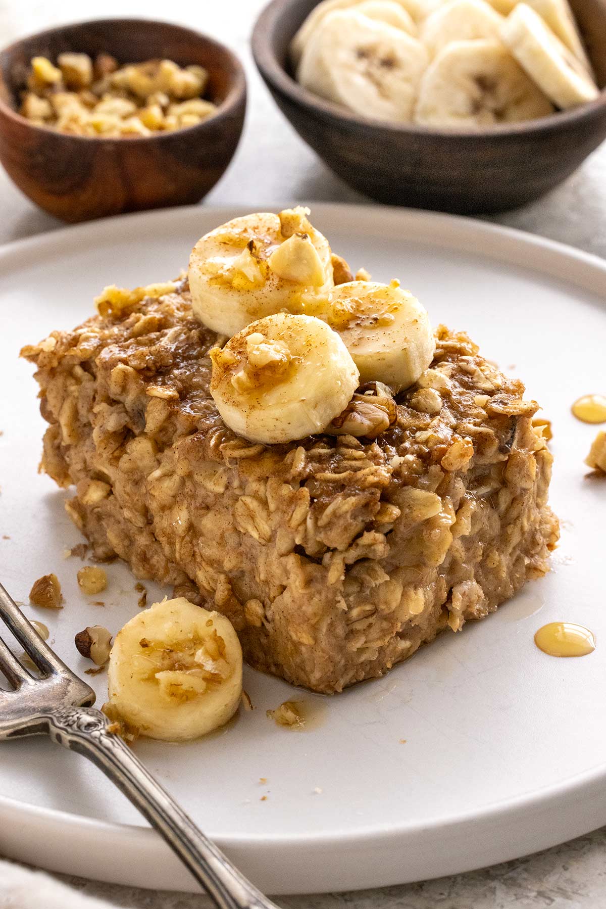 Piece of baked oatmeal with slices of banana on top served on a white plate.
