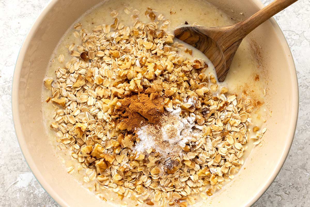 Chopped walnuts, spices, and rolled oats in a mixing bowl with a wooden spoon.