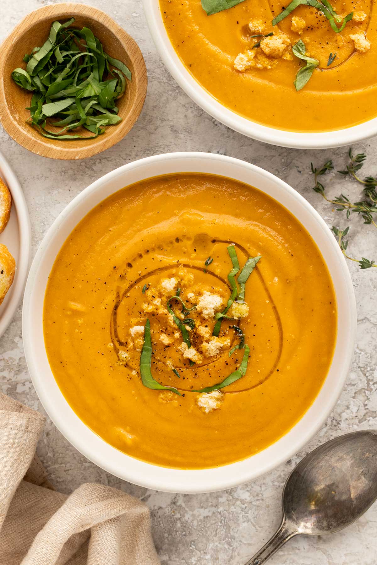 Two bowls of roasted vegetable soup garnished with basil and breadcrumbs.