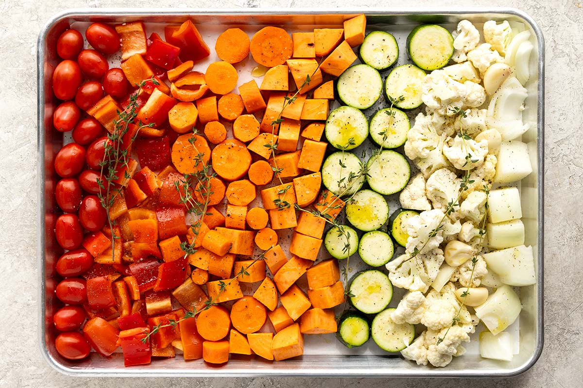 Tomatoes, peppers, carrots, zucchini, and cauliflower florets placed on a sheet pan.