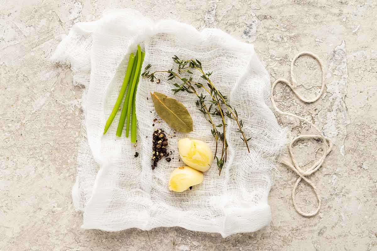 Cheesecloth cut into a square with spices and garlic cloves placed on top.