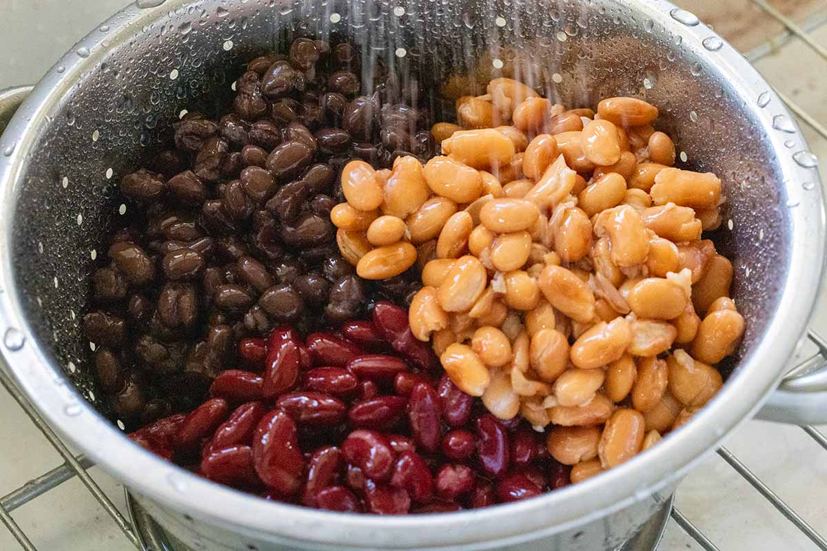 Black beans, pinto beans, and kidney beans in a colander being rinsed with water.