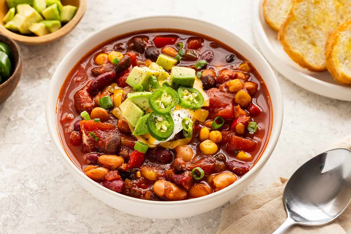 Bowl of vegetarian chili topped with garnishes and served with pieces of bread on the side.