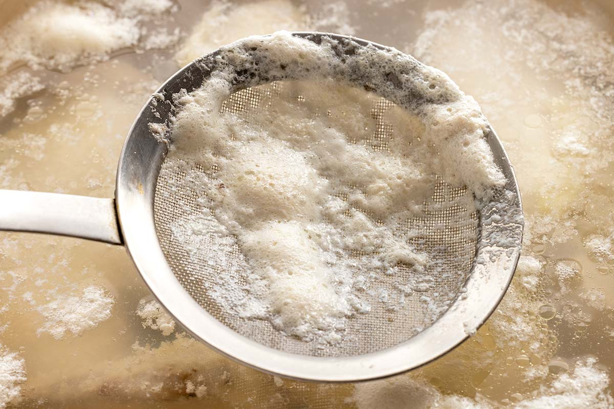 Fine mesh strainer with scum on it after straining chicken simmering in a pot.