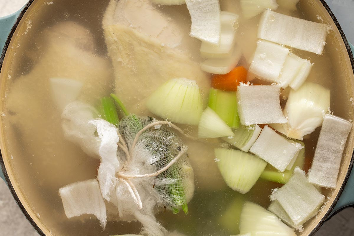 Chicken, carrots, onions, celery, and a bag of spices simmering in a pot.