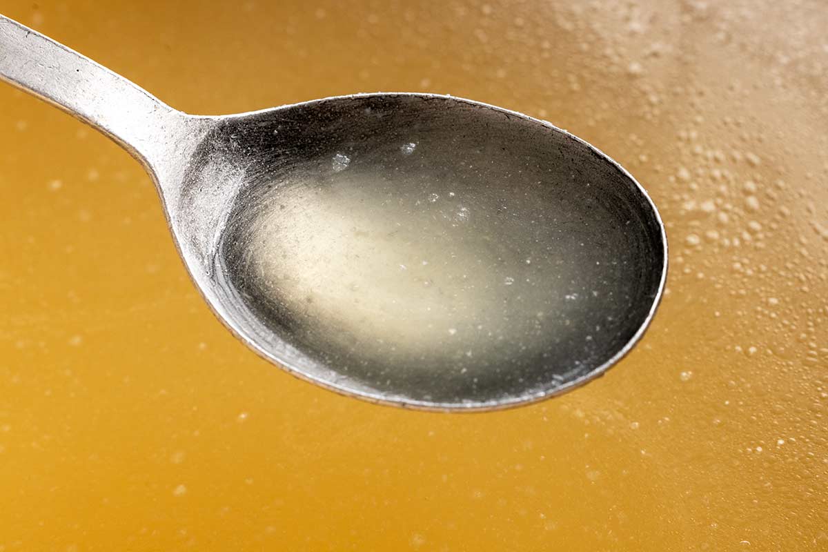 Metal spoon showing the clarity of homemade chicken broth.