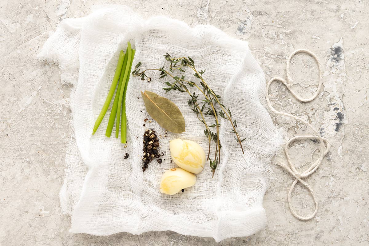 Thyme, peppercorns, garlic, and baf leaf on a piece of cheesecloth.