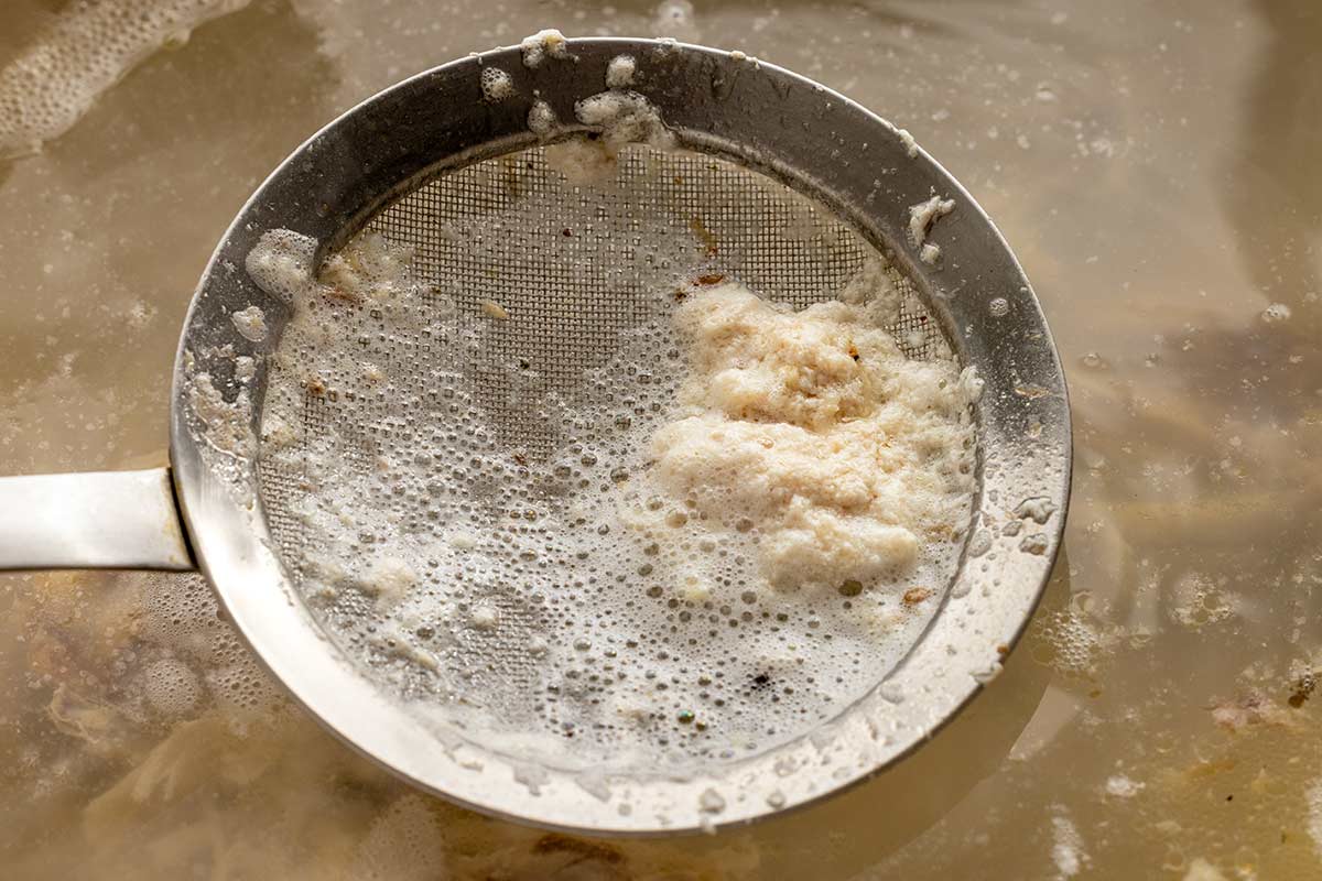 Strainer scrapping fat off water.