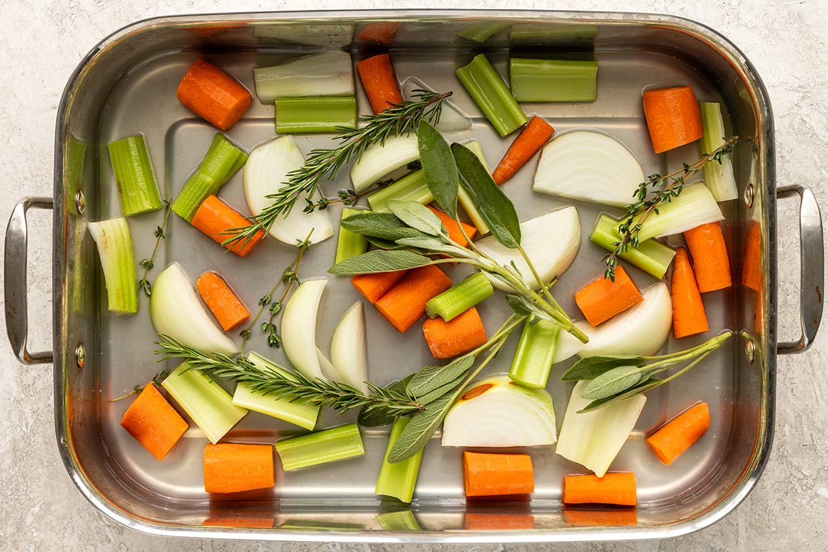 Roasting pan with pieces of carrots, onions, rosemary, thyme, and celery.