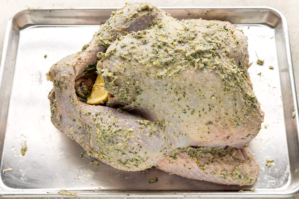 A whole turkey covered in compound butter and placed on a sheet tray.