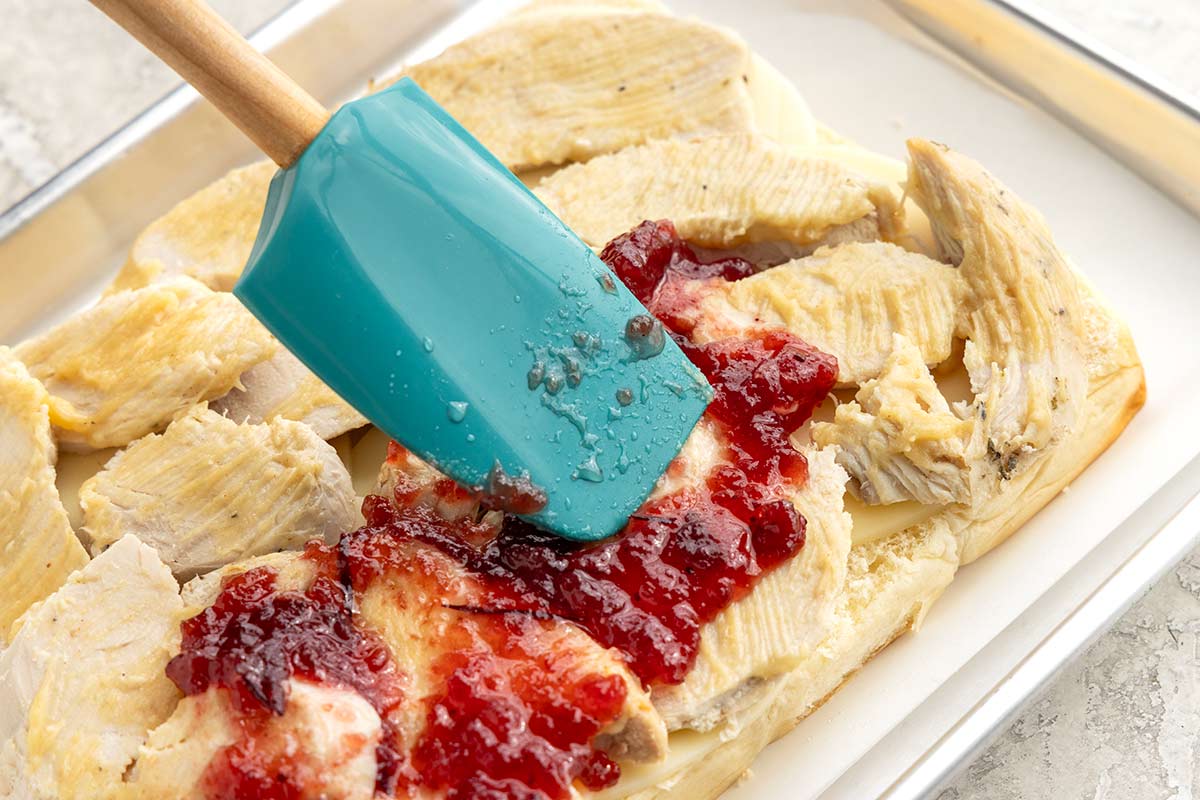 Spatula spreading cranberry sauce over the top of sliced turkey.