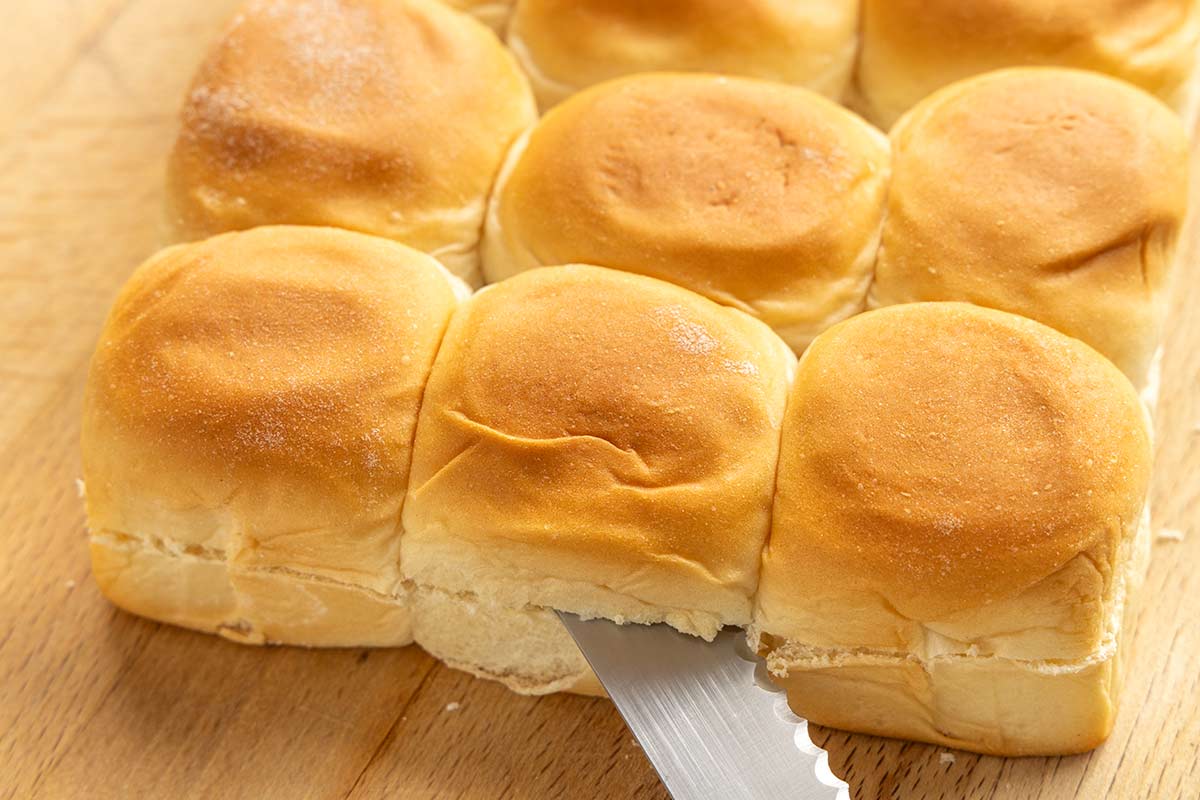Hawaiian rolls being cut in half with a serrated kitchen knife.