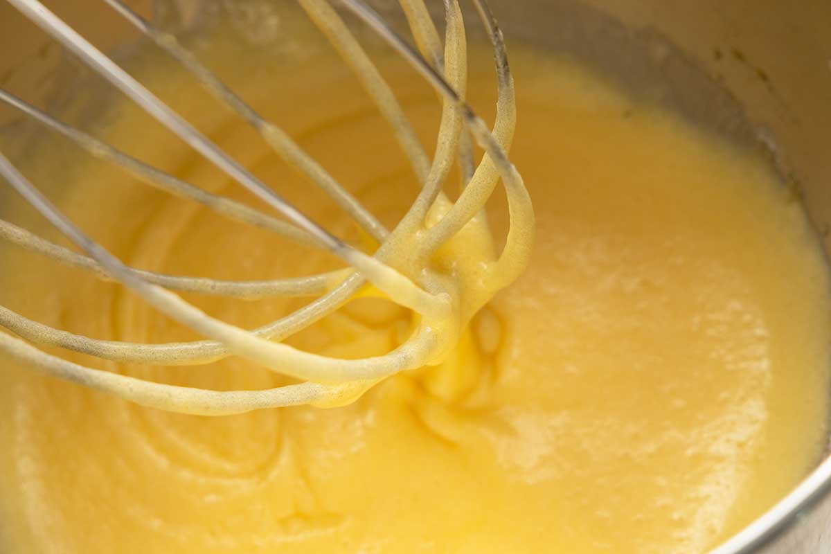 Close up of a whisk attachment inside a stand mixer bowl with eggs.