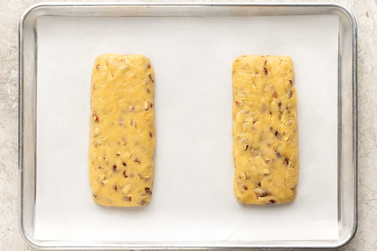 Two portions of biscotti dough on a paper lined sheet pan.