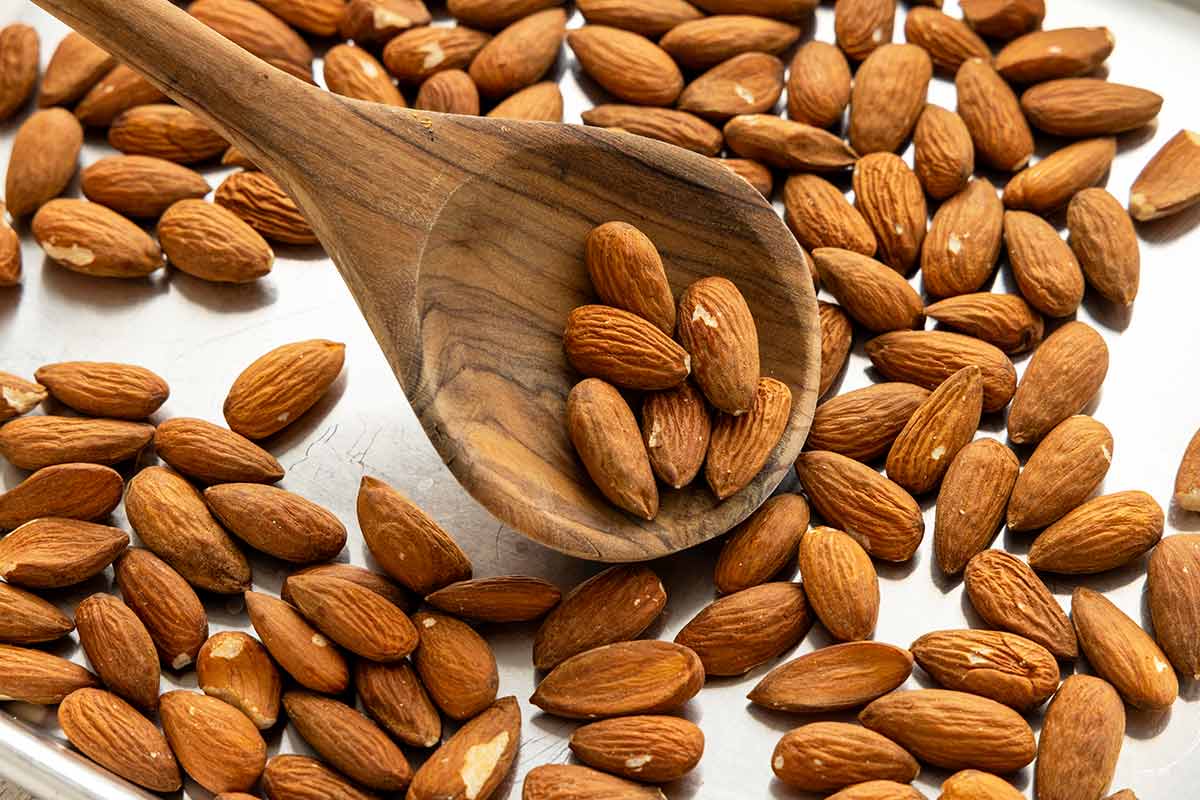Wooden spoon flipping toasted almonds on a sheet pan.