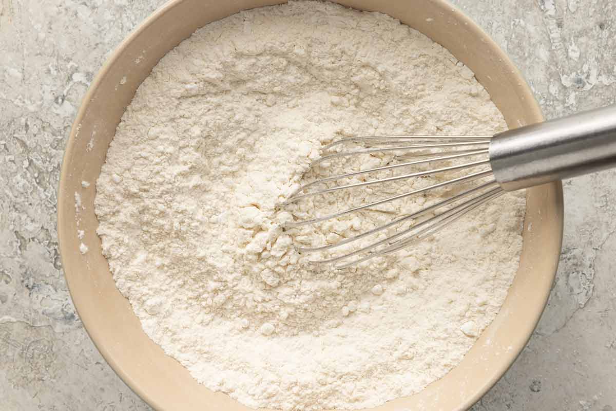 Flour and powdered sugar in a mixing bowl with a whisk in the center.