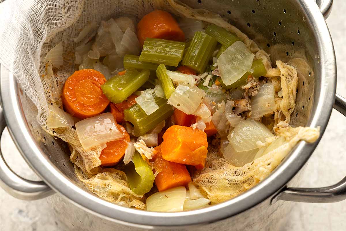 Chunks of carrots, celery, and onions caught in a cheescloth after being strained.