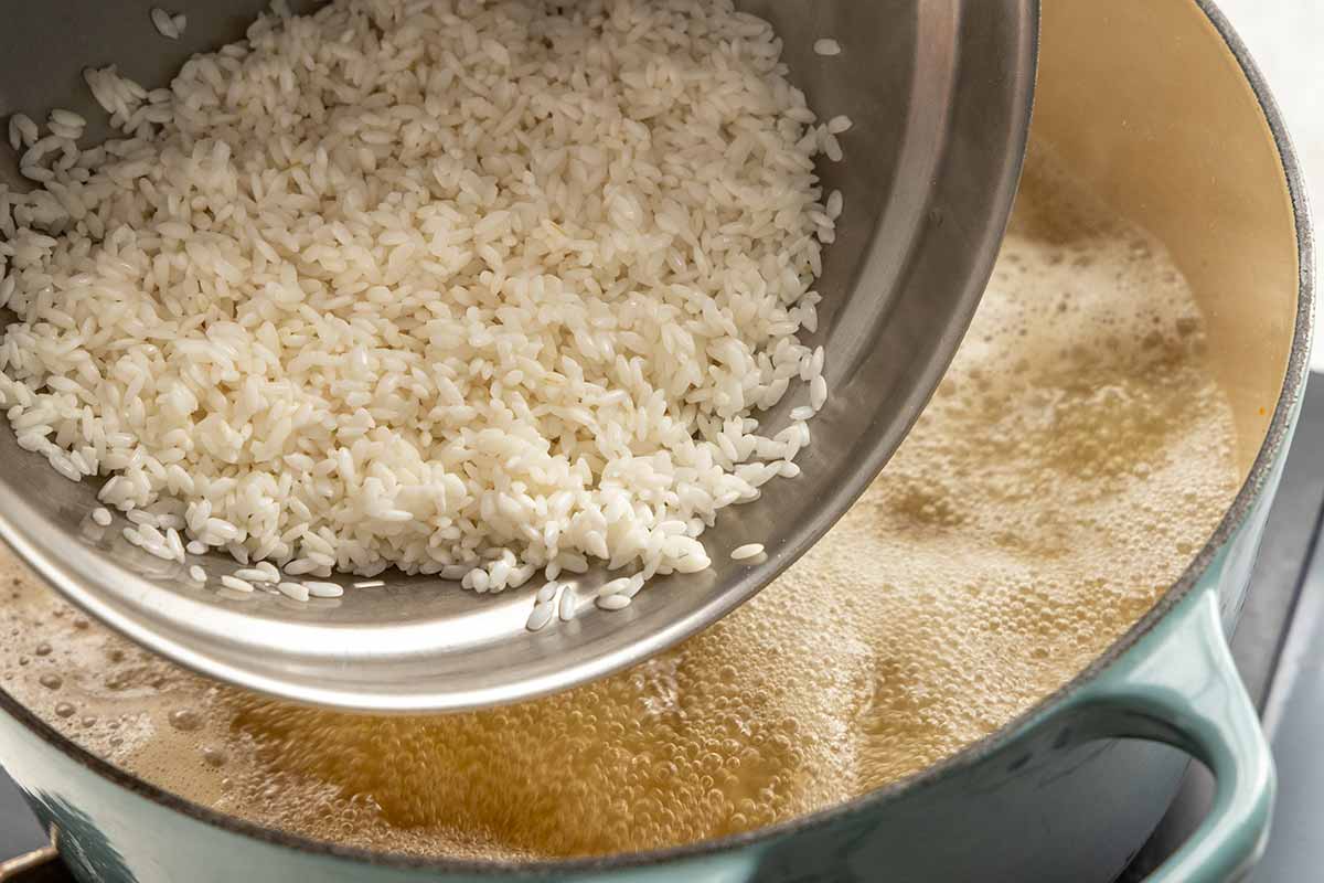 Bowl of white rice being poured in a pot of bubbling turkey stock.
