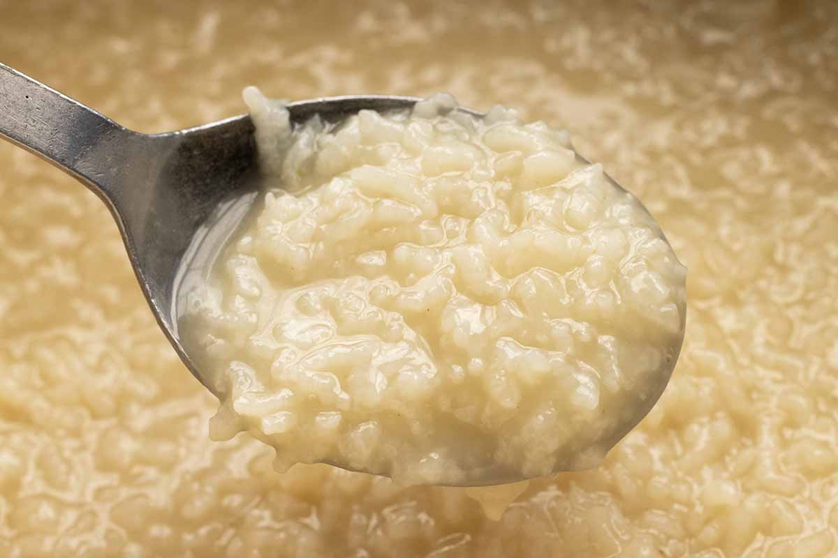 Spoon lifting cooked white rice out of a pot.