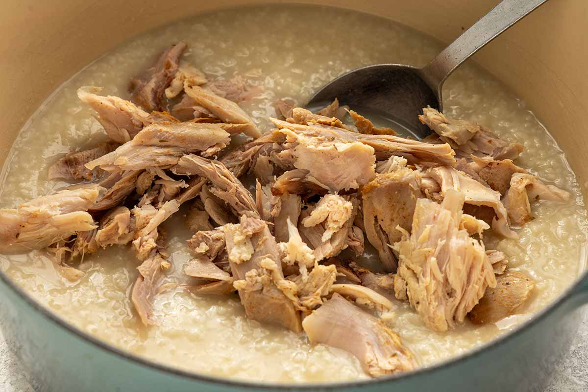 Shredded turkey being added to a pot of rice porridge.