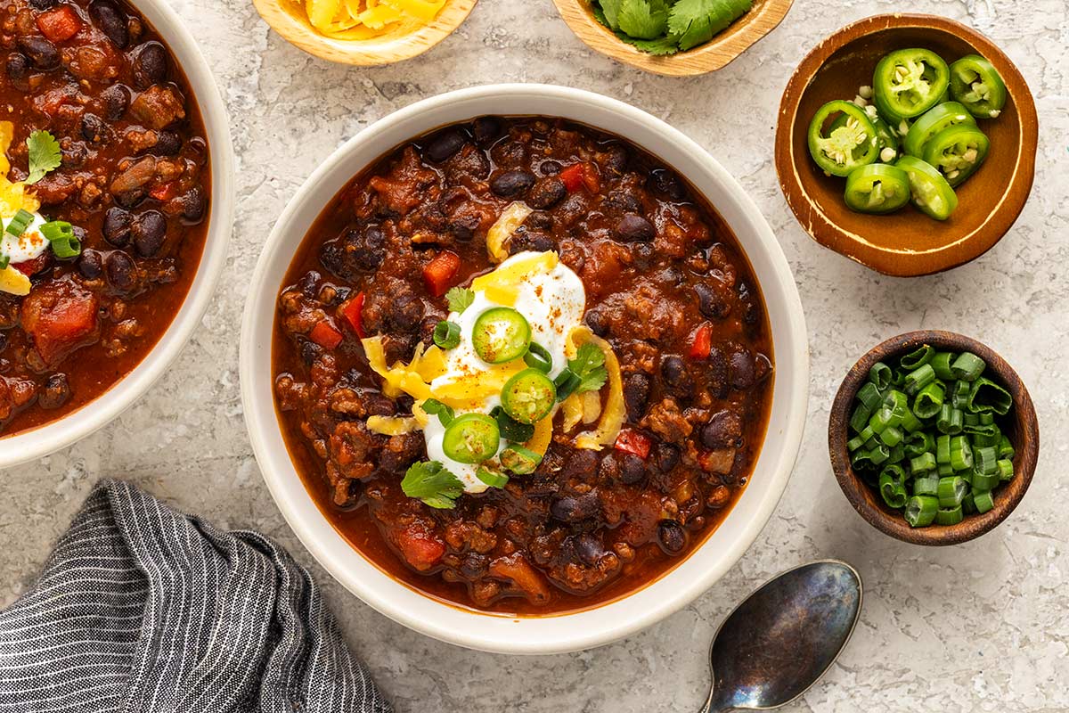 Two bowls of chili placed next to smaller balls with toppings.