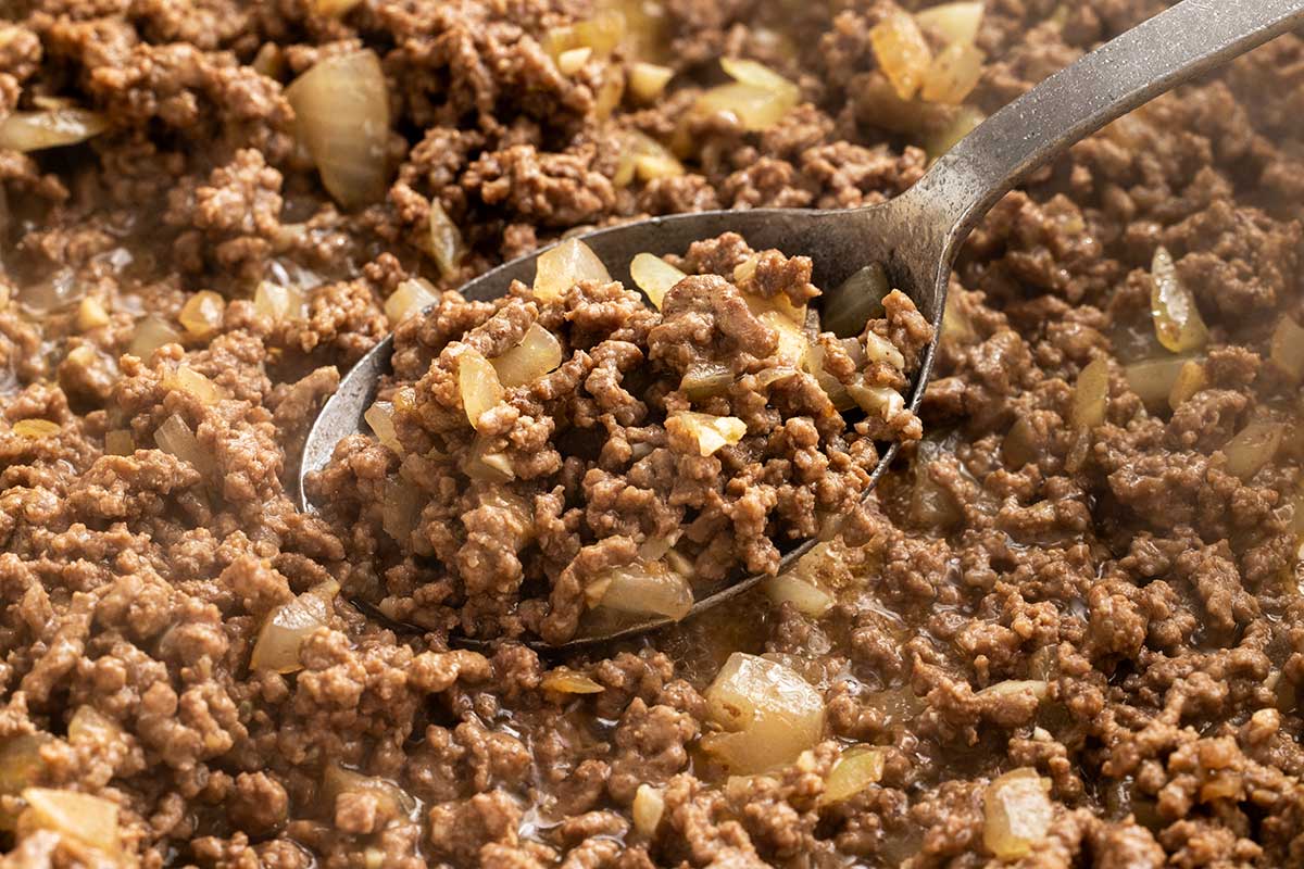Metal spoon mixing ground beef in a pan.