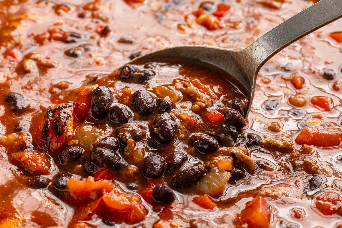 Pot of black beans and canned tomatoes being mixed around with a metal spoon.