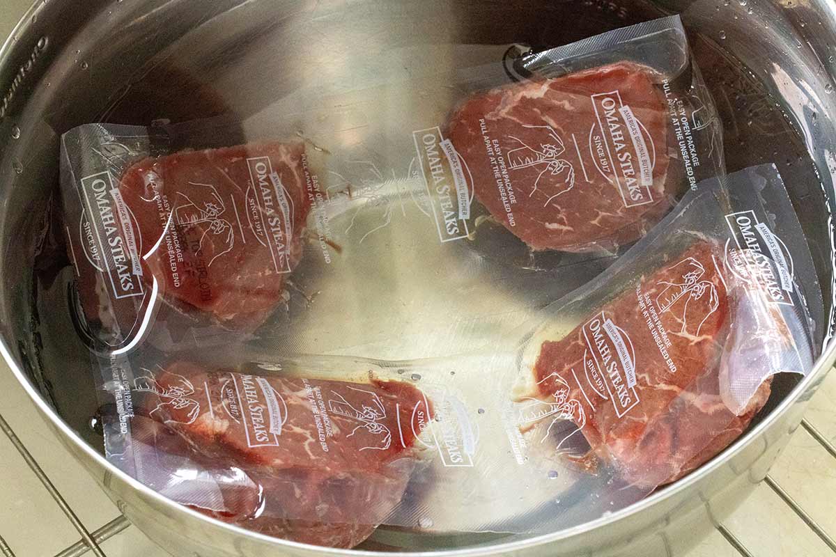 Packages of Omaha steak filets thawing in a bowl of water.
