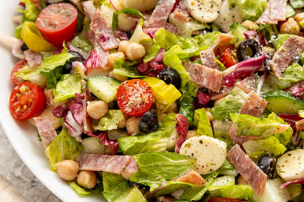 Slices of salami, mozzarella, chickpeas, and olives tossed in a salad.
