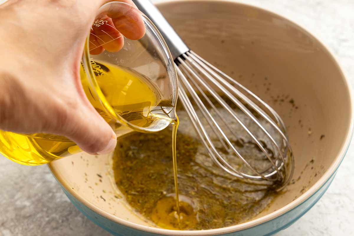 Jessica pouring olive oil slowly into a bowl of salad dressing.
