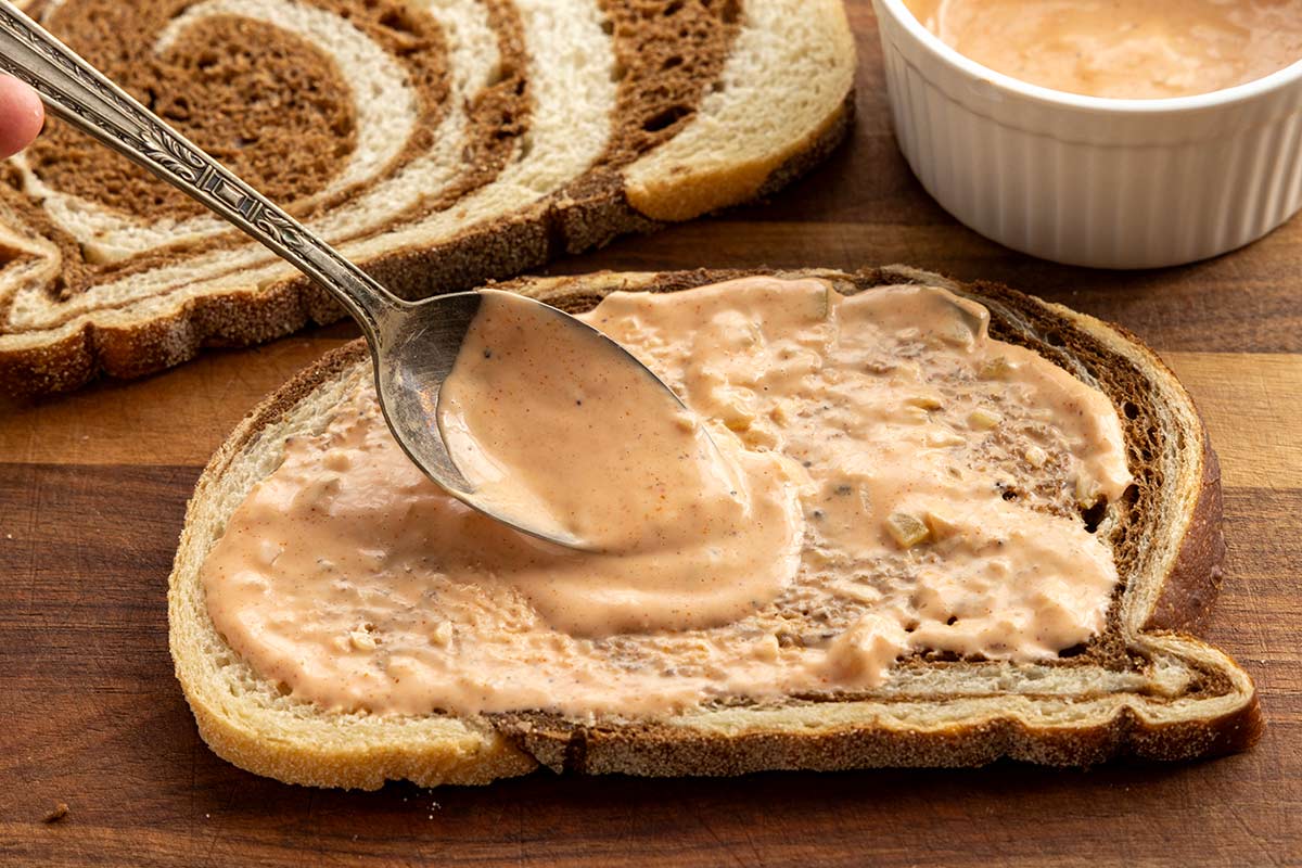 Spoon spreading Russian dressing on a slice of marble rye bread.