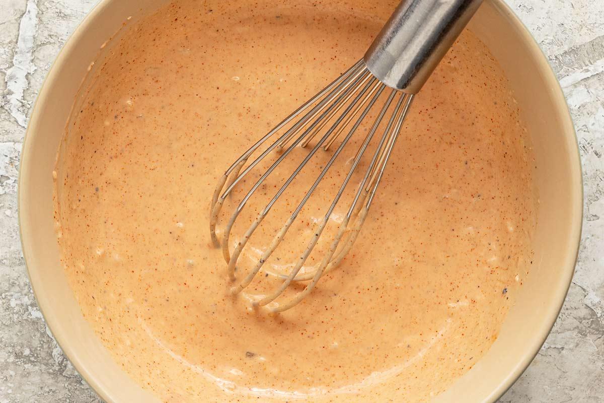 A whisk inside a bowl after mixing together Russian dressing ingredients.