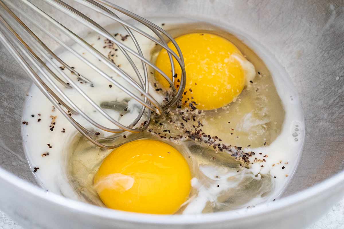 Two eggs in a mixing bowl with salt, pepper, and a whisk.