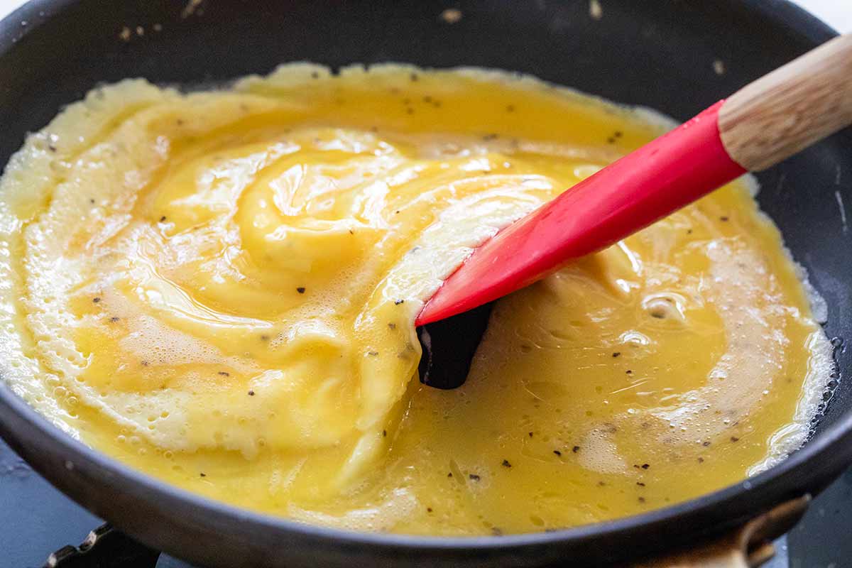 Spatula moving scrambled eggs around in a pan.