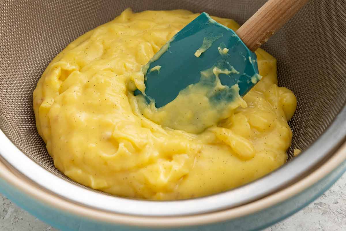 Spatula pressing pastry cream through a strainer.