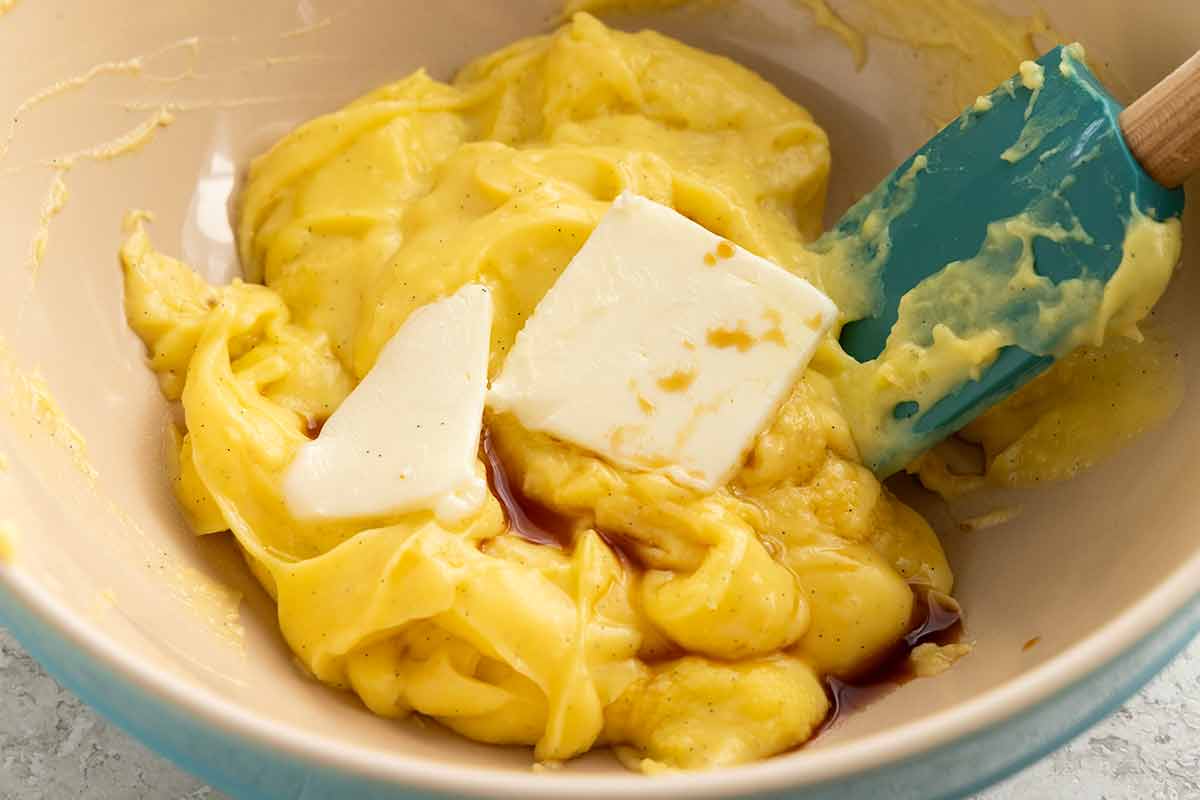 Butter being incorporated into a bowl of pastry cream.