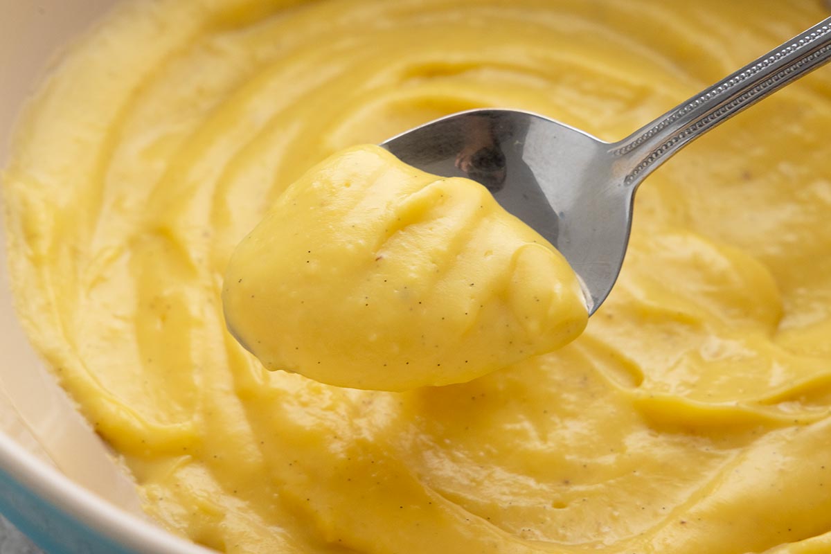 Metal spoon lifting pastry cream out of a bowl.