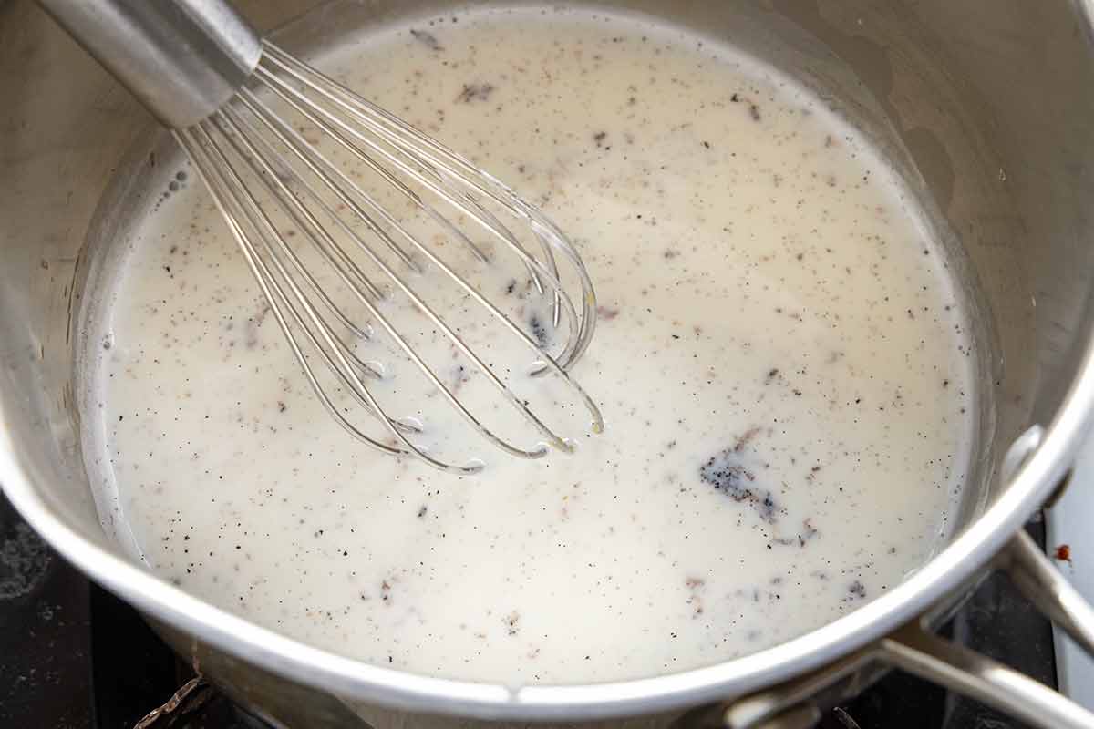 Pot of milk and vanilla bean being whisked.