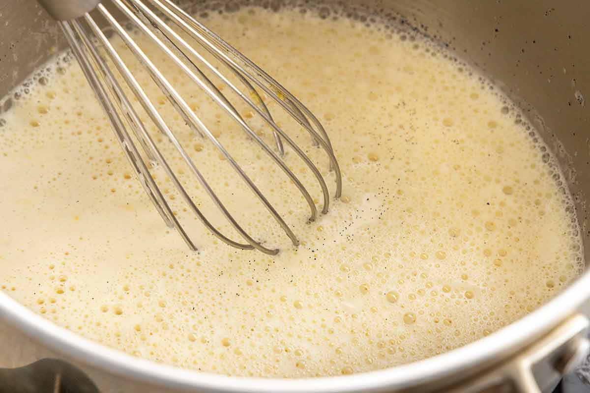 Foam forming on top of egg yolks being heated in a saucepan.