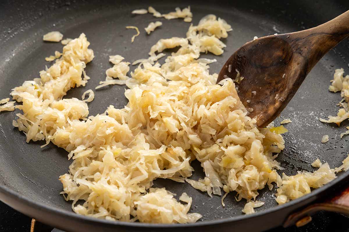 Spoon moving sauteed sauerkraut on a pan.