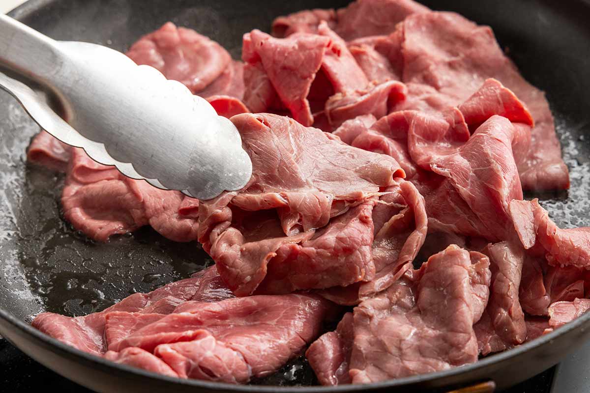 Metal tongs flipping pieces of corned beef in a saute pan.