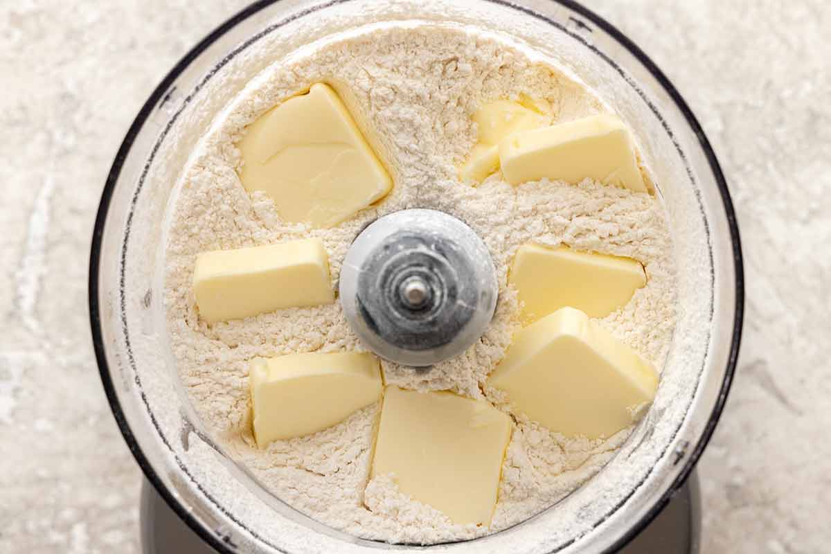Slices of butter placed in a food processor with flour.
