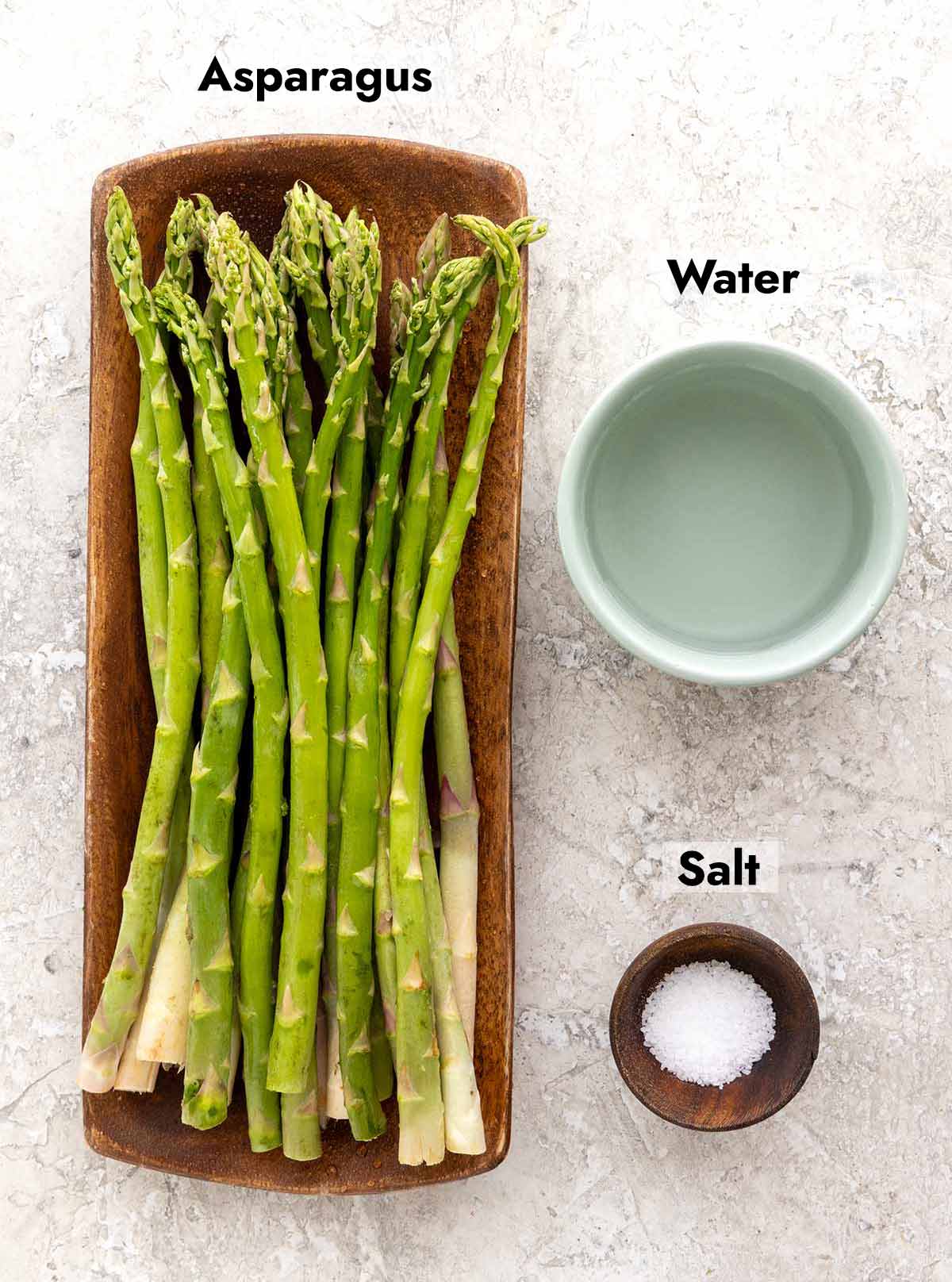 Asparagus on a wooden plate, small bowl of water, and a tiny wooden bowl of salt.